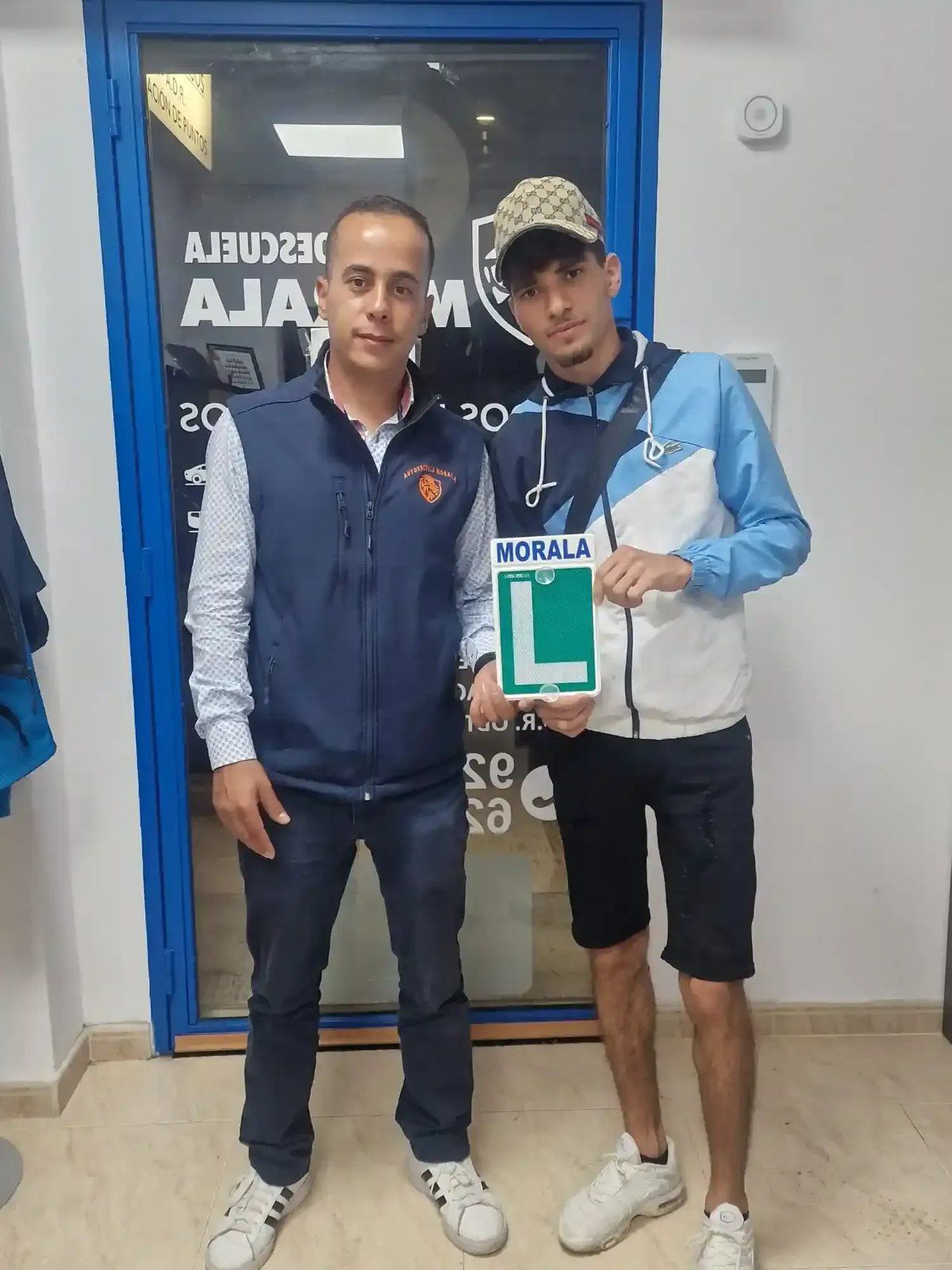 Alumno aprobado con la placa L de Morala junto a su profesor, en la puerta de la autoescuela