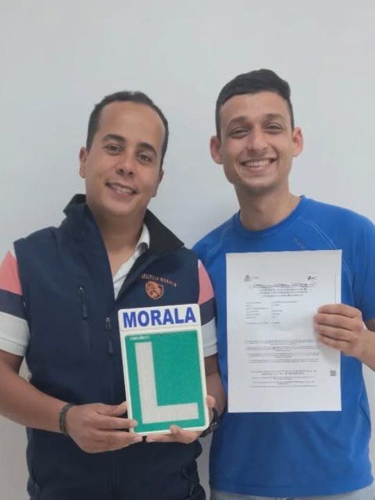 Alumno aprobado con la placa L de Morala y su resultado del examen, junto a su profesor